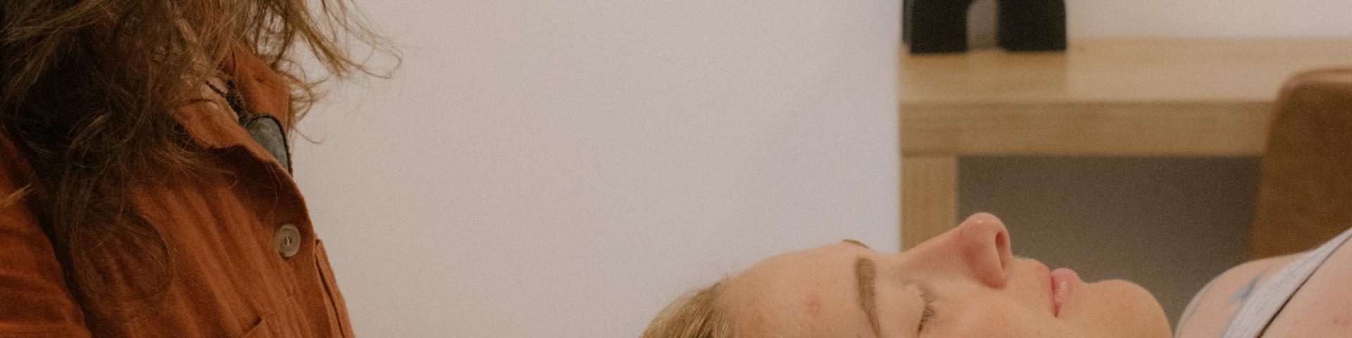 Craniosacral Therapy session showing Cedra Woods gently supporting a client’s head while they lie on a treatment table in a calm, minimalist healing space.