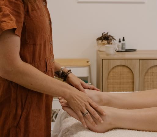 Craniosacral Therapy session showing Cedra Woods palpating at the client’s feet while they lie on a treatment table in a calm, minimalist healing space.