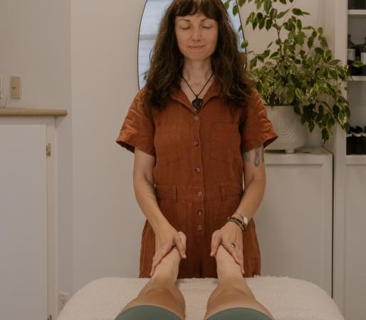 Craniosacral Therapy session showing Cedra Woods palpating at the client’s feet while they lie on a treatment table in a calm, minimalist healing space.