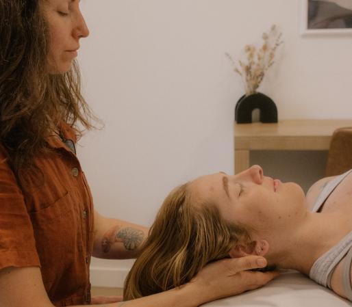 Craniosacral therapy session showing Cedra Woods gently supporting a client’s head while they lie on a treatment table in a calm, minimalist healing space.