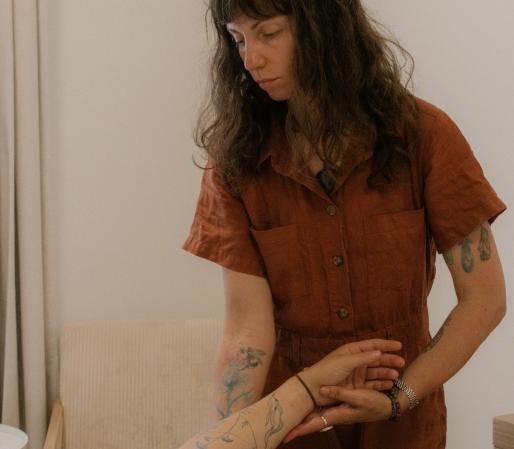 Craniosacral Therapy session showing Cedra Woods unwinding a client’s arm while they lie on a treatment table in a calm, minimalist healing space.