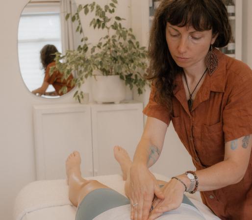 Craniosacral Therapy session showing Cedra Woods performing visceral manipulation on a client's abdomen while they lie on a treatment table in a calm, minimalist healing space.