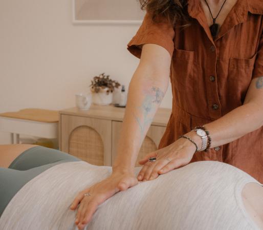 Craniosacral Therapy session showing Cedra Woods performing visceral manipulation on a client's abdomen while they lie on a treatment table in a calm, minimalist healing space.