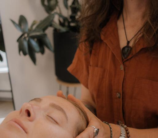 Craniosacral Therapy session showing Cedra Woods performing Craniosacral Therapy on a client's brain with hands cupped around their head while they lie on a treatment table in a calm, minimalist healing space.
